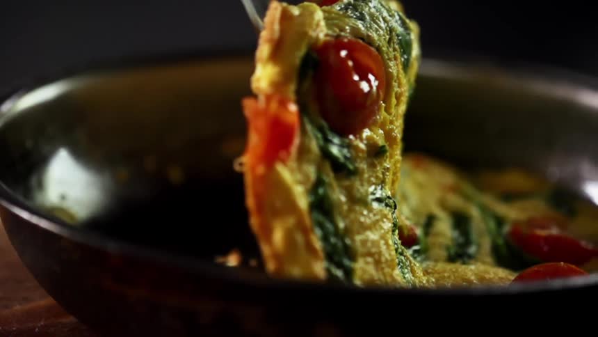 The omelette with spinach and tomatoes is flipped in the pan