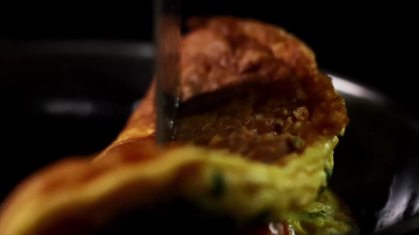 An omelette with tomato and greens is folded in half in a pan
