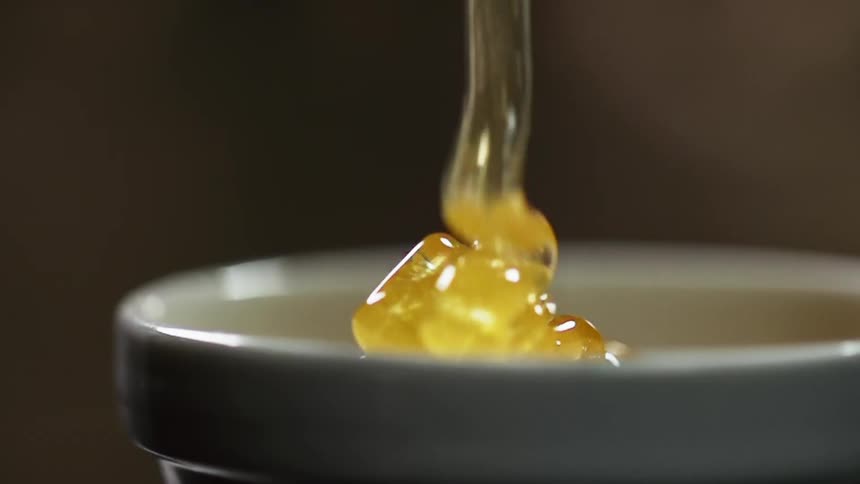 Honey pours and pools into a small white bowl