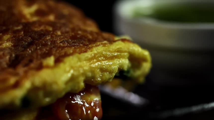Filled omelette being served on a black ceramic dish near green sauce