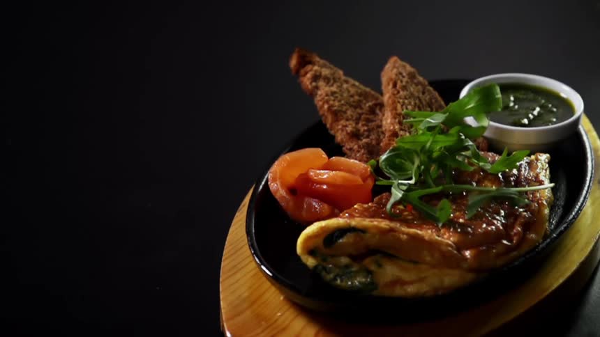 Greens are added to a plate of omelette, salmon and bread