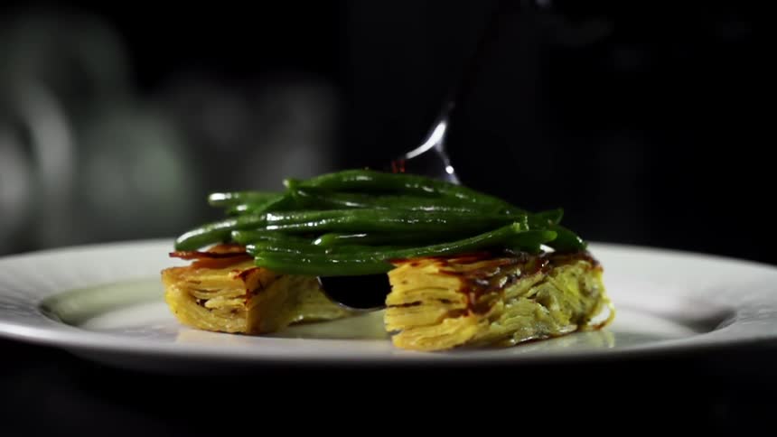 A spoon placing vegetables on top of a pastry on a plate that is on a table