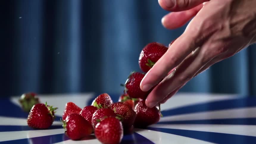 A person placing strawberries on a table with their hands
