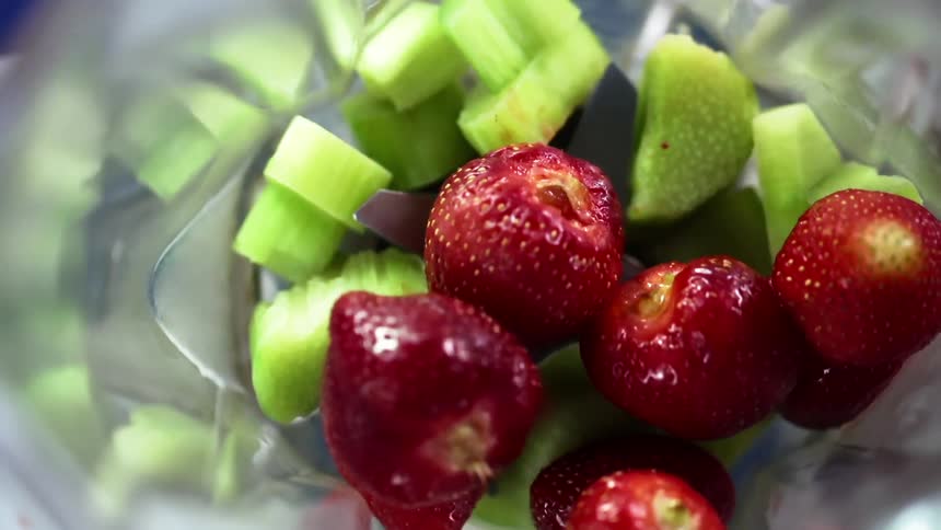 Strawberries dropping onto chunks of kiwi in a blender