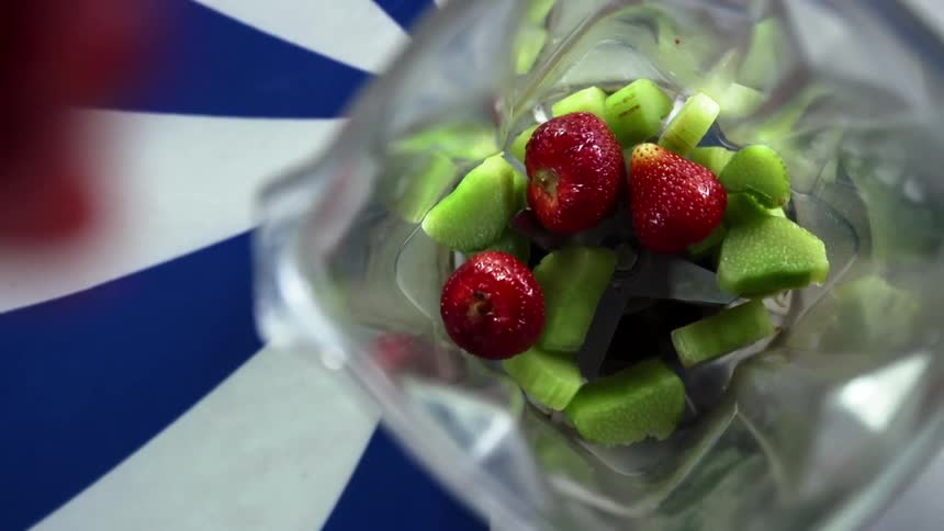 Strawberries being poured into a blender already containing sliced vegetables