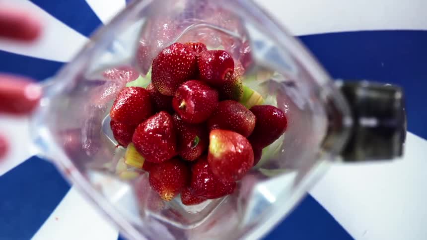 Fresh red strawberries piling up inside the glass jar of a mixer