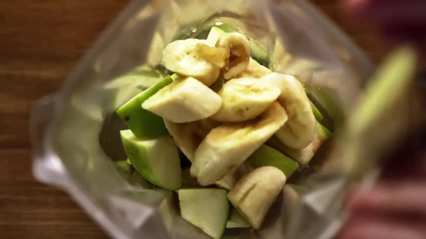 A person putting apples and bananas in a blender
