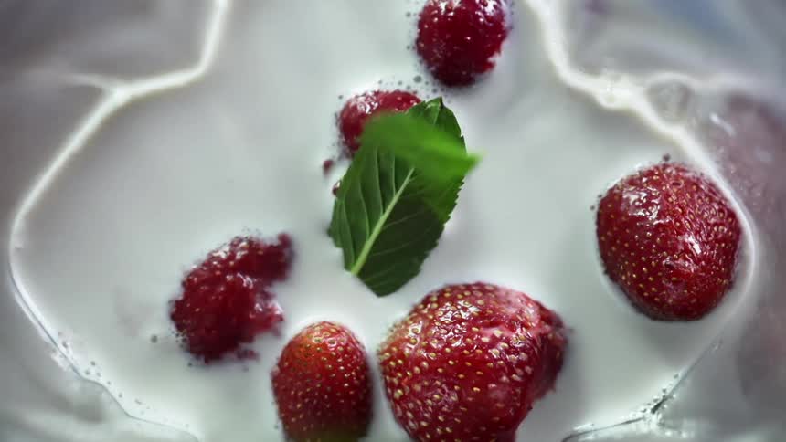 Green leafs falling over red fresh strawberries floating in cream