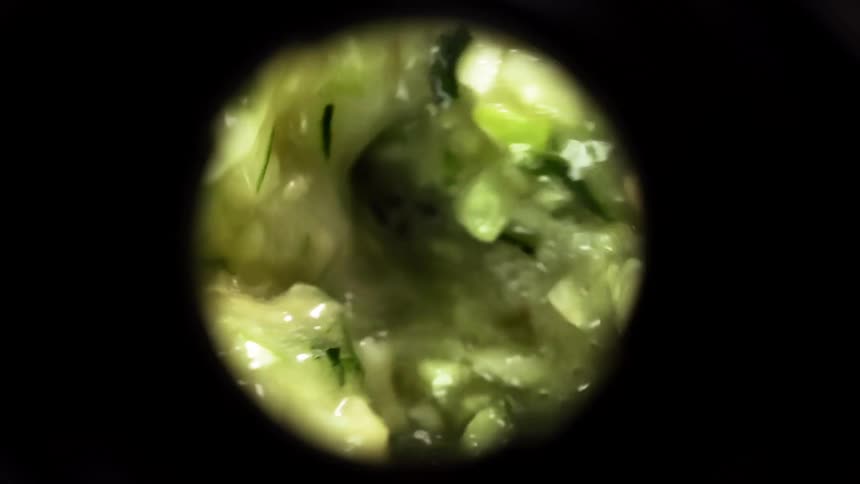 A view inside of a blender from above shows spinach leafs and other vegetables chopped and blended together