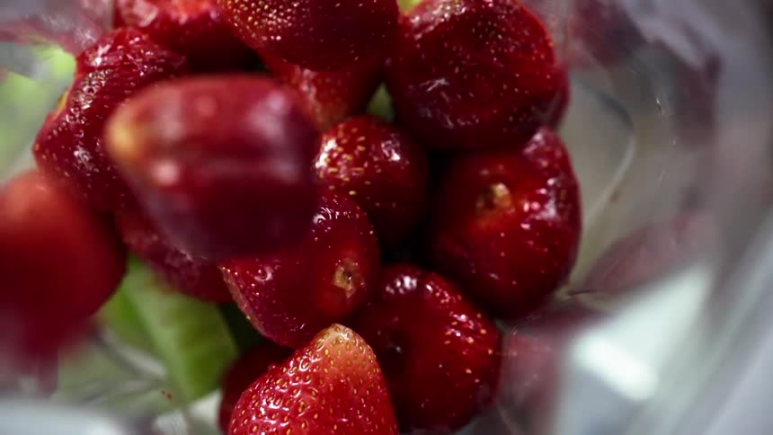Strawberries drop into a pile in a clear container