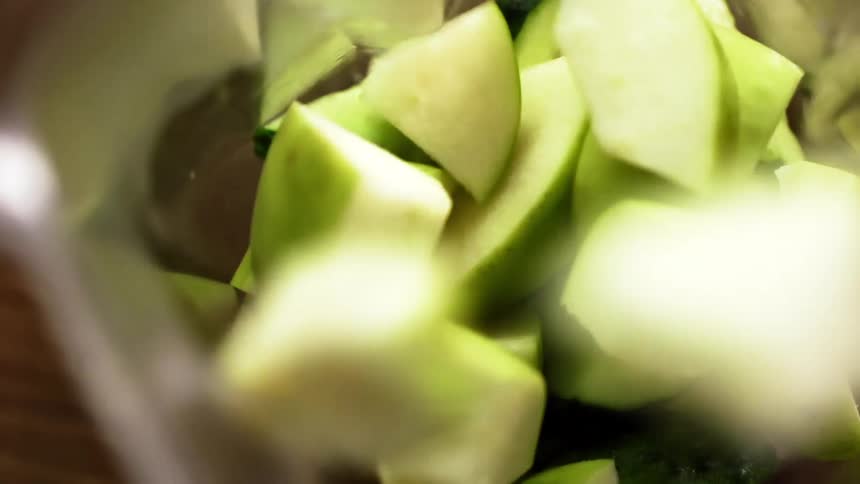 Sliced pieces of avocado are dumped atop a pile of cucumbers in a transparent container