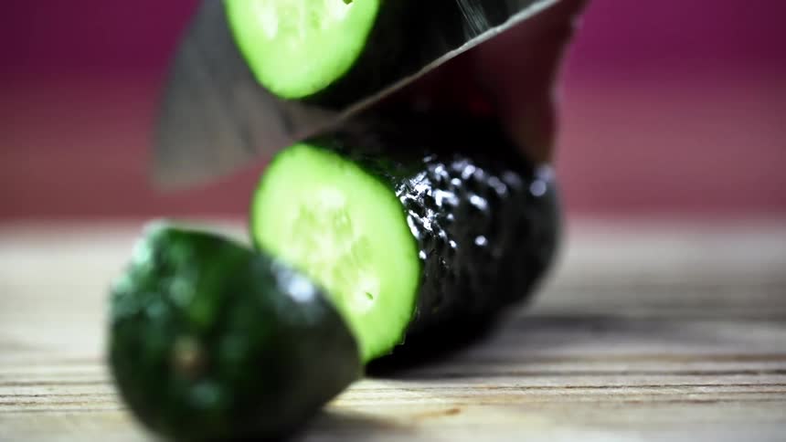 A holds a cucumber on a cutting board and cuts several cucumber slices using a knife