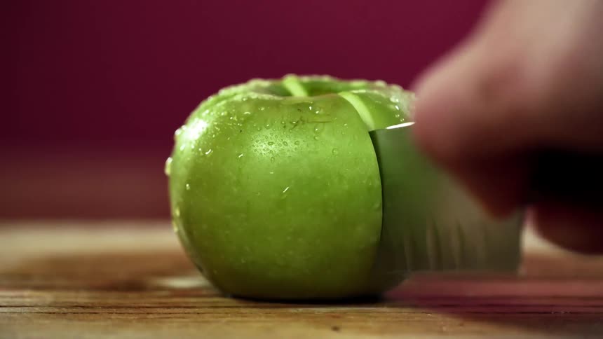 Close up of a mans hand cutting a green apple in half with a sharp knife