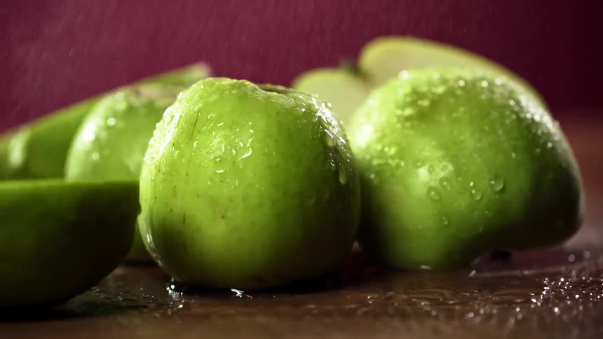 Halves of green apples being sprayed with water as they lie on a table