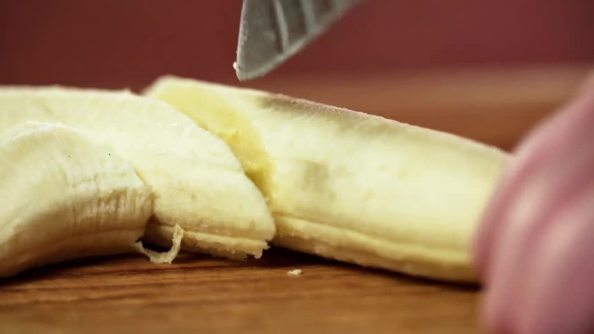 A white person slices a banana with a knife