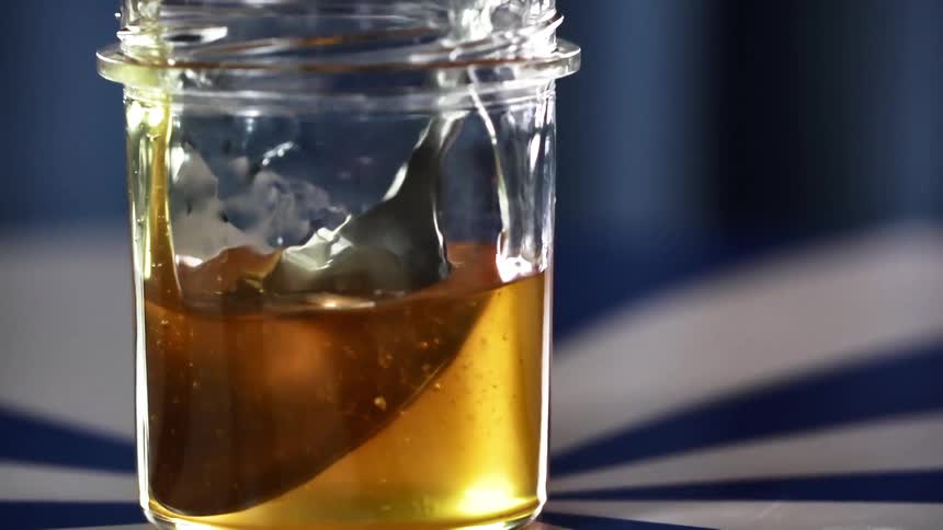 A hand holding a spoon gets honey out of a jar