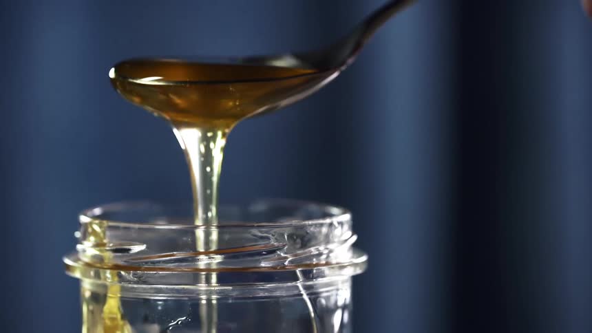 A white person lifts a spoon of honey out of a jar