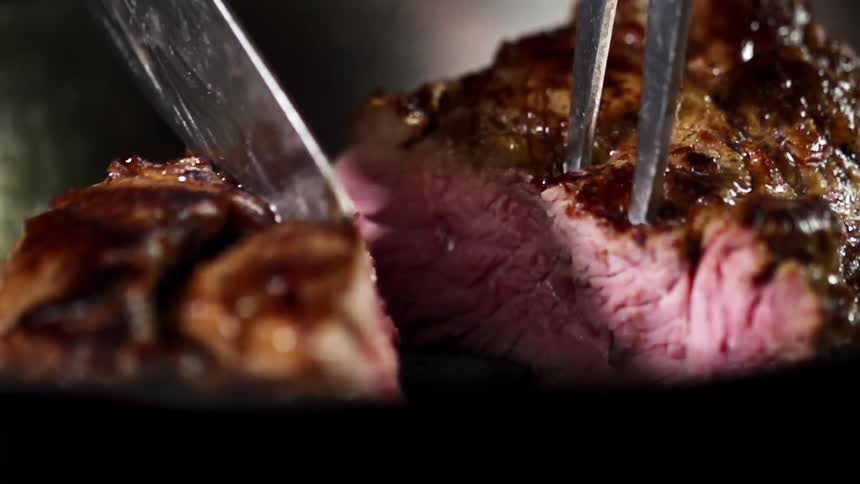 Two halves of a steak being pushed apart by a knife and a grill fork