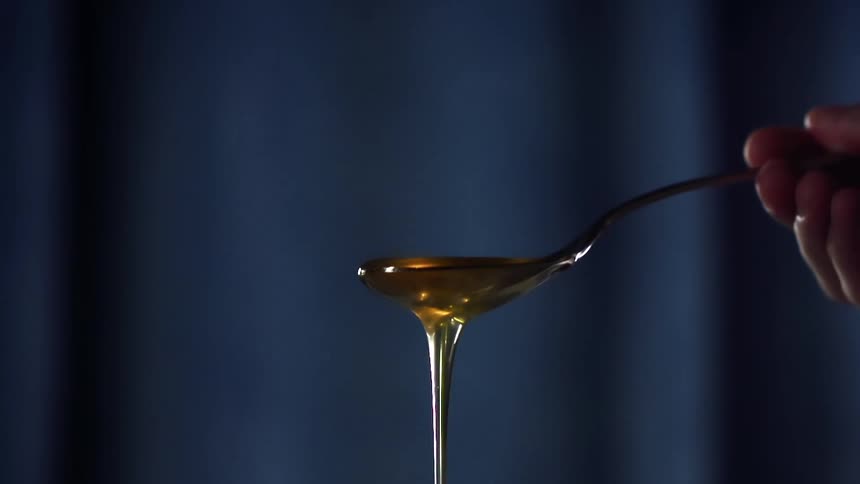Gold honey is spooned out of a glass jar