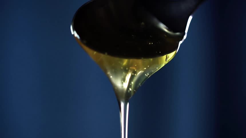 A spoon scoops oil from a glass before tilting to let the oil pour back into the glass