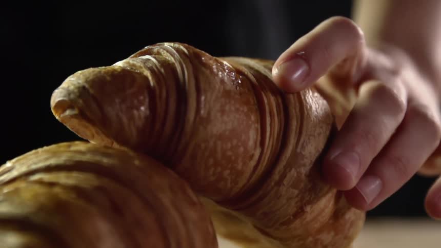 Hand placing croissant on top of another croissant in slow motion