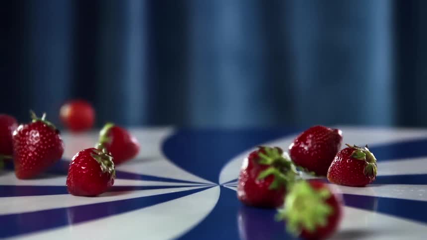 A number of strawberries tumble across a counter top