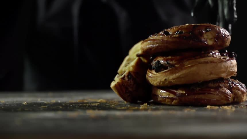 A gloved hand places a cinnamon roll on top of others