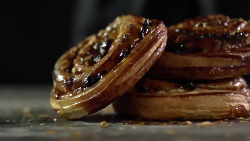 A glazed pastry falls onto a stack of two similar glazed pastries