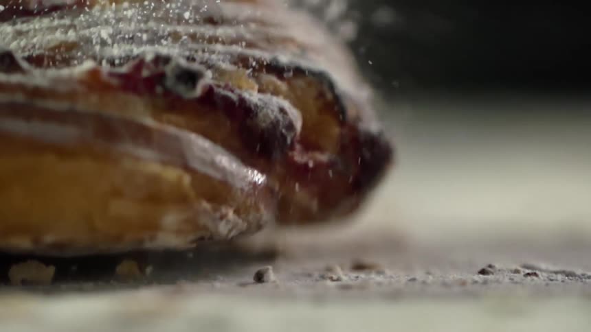 A pastry covered in powdered sugar falls onto a tabletop covered in sugar and crumbs