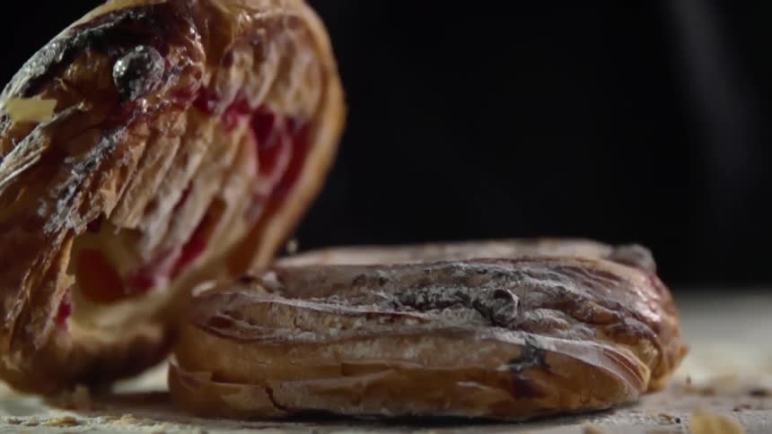A bread pastry drops on another pastry in a spray of crumbs and flour