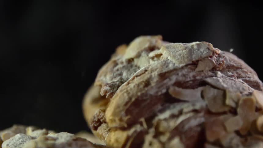 A roll of bread covered in shaved nuts drops onto a pile of food