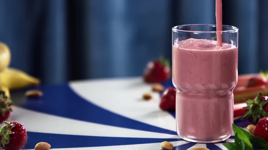 Pouring a strawberry and banana smoothie in a glass on a spiral table
