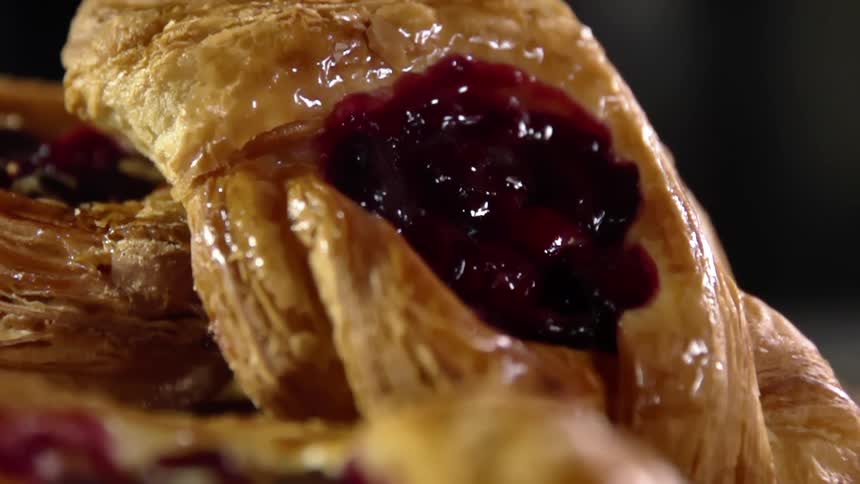 A jam filled and flaky baked pastry is placed on top of a pile of others