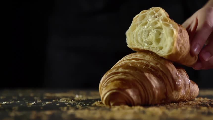 A croissant that is sliced in half is carefully placed atop another flaky croissant