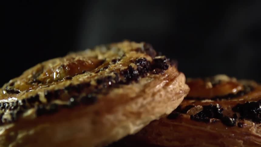A pastry roll with blackberries and almond slices is dropped onto a surface