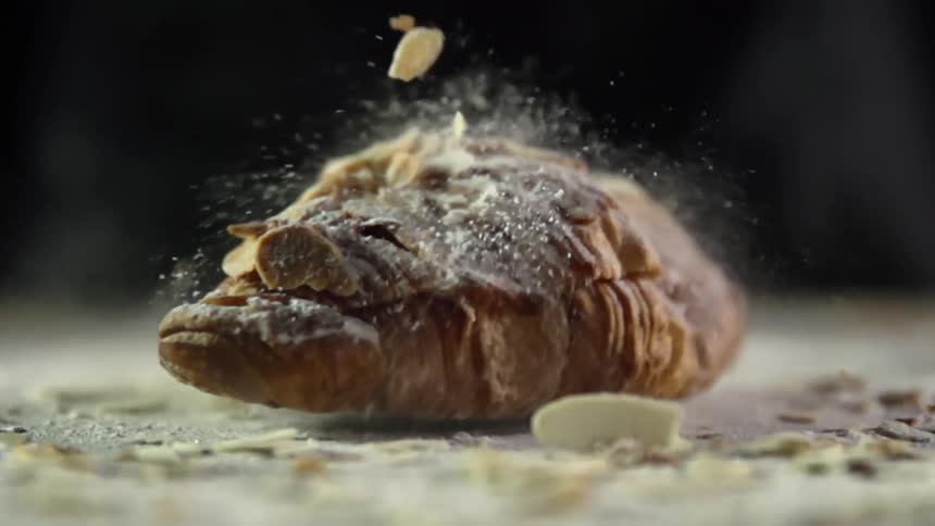 A bread pastry covered in nuts drops on a table
