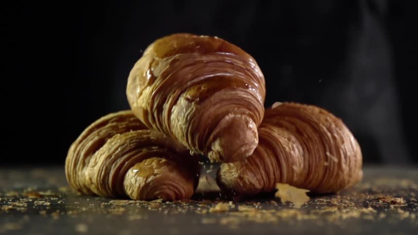 Croissant falls over other croissants in a table breaking some crumbs