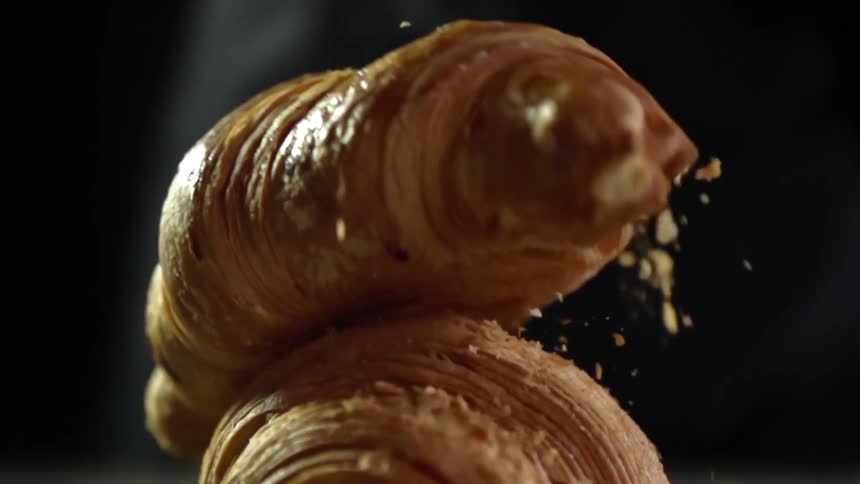 A buttery croissant is dropped onto another causing to flake as it lands