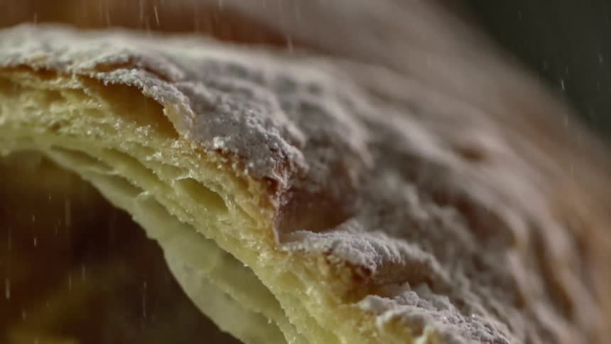 Confectioners sugar falls over the surface of an open croissant