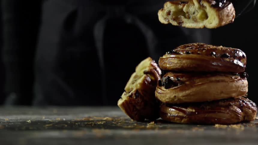A person wearing a black glove sets a bread pastry on a pile of pastries