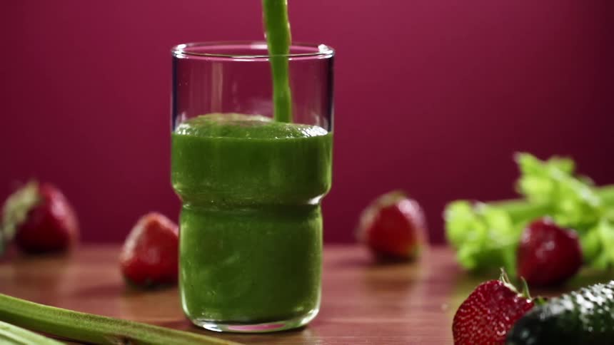 A clear glass is filled with thick green juice from a pitcher