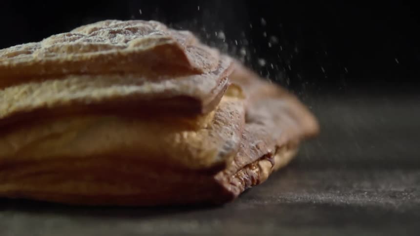 A pastry covered in powdered sugar falls onto a table causing sugar to scatter around the tables surface