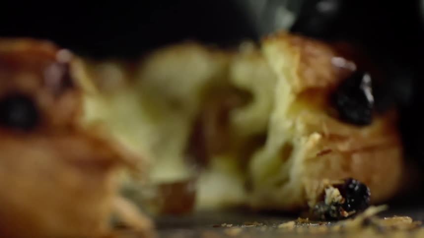 Chef wearing black latex gloves cuts a sweet roll filled with fruit with a sharp kitchen knife