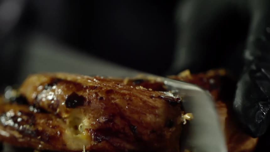 Chef with black latex gloves cuts a sweet roll in half with a serrated kitchen knife