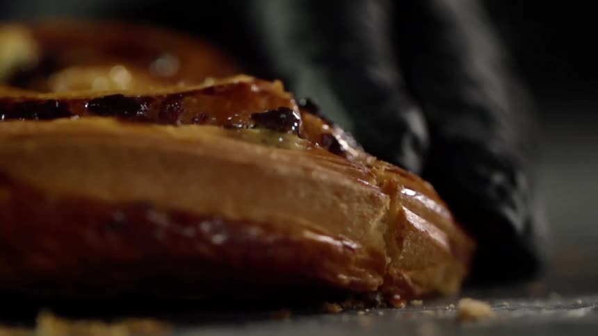 A black gloved figure slices a pastry with a serrated knife