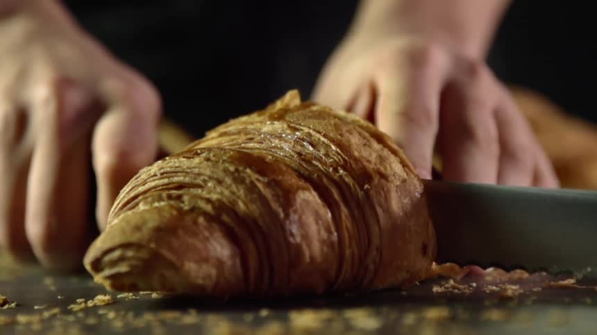Man cuts a crumbling croissant with a serrated kitchen knife