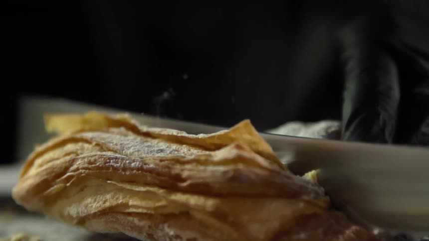 Person in black gloves cuts flaky pastry with knife