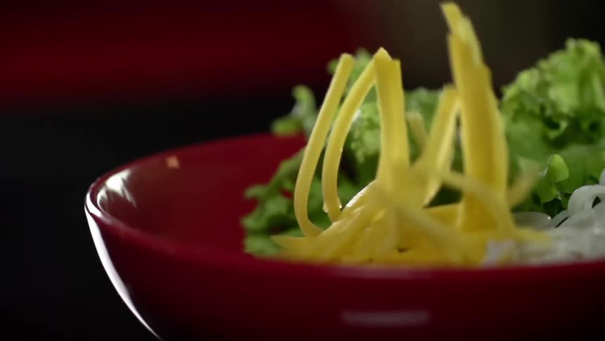 Shredded cheese falls into a salad bowl