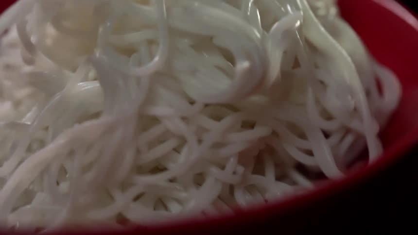 Noodles fall into a red bowl of noodles and bounce before settling