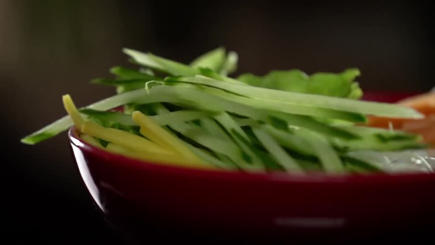 A bundle of greens falls into a bowl filled with salad